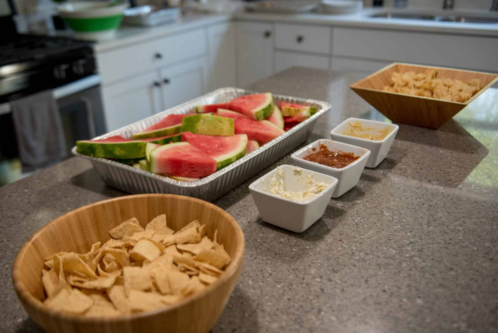 Chips and dip next to a bowl of watermelon on a countertop