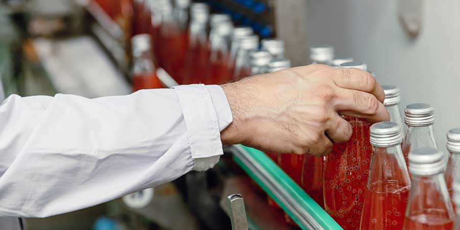 Hand On Bottles On Conveyor Line With Red Liquid