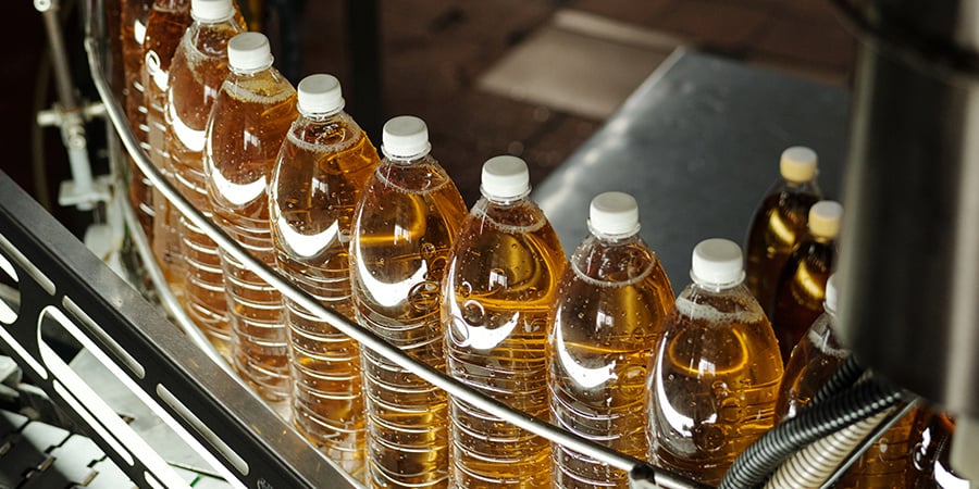 Clear bottles with golden liquid on a curved portion of the production line. 