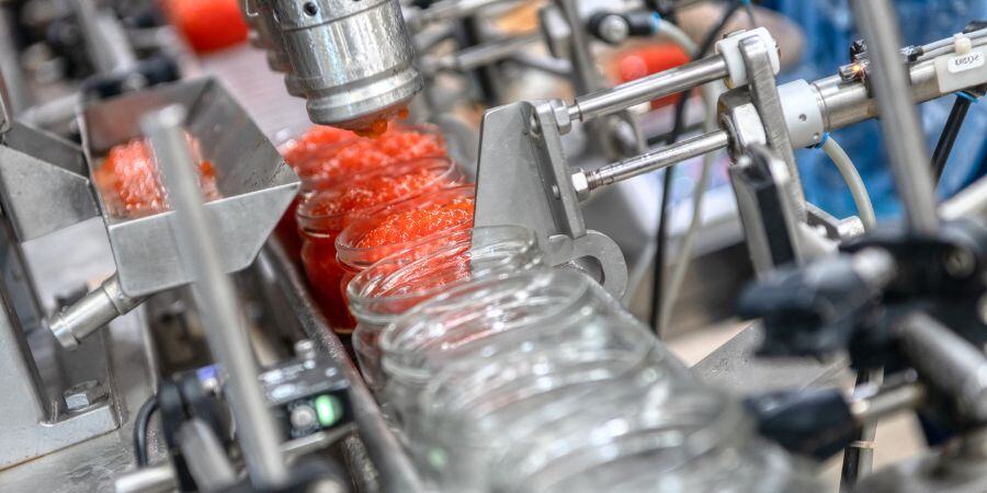 Filling machine filling glass jar with orange semi-liquid product