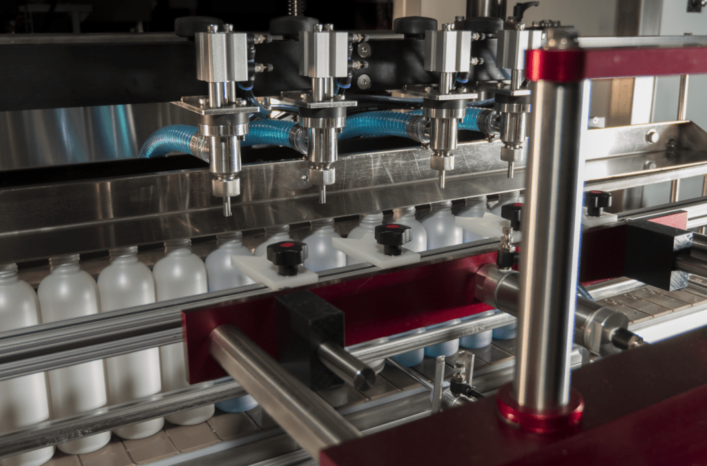 A 4 Head Pump Filler hovers over bottles on a conveyor ready to be filled